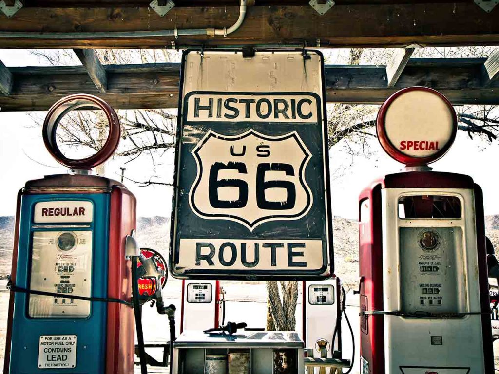 Distributori di carburante dallo stile vintage accanto a un cartello che indica il percorso dell'Historic Route 66 negli USA.
